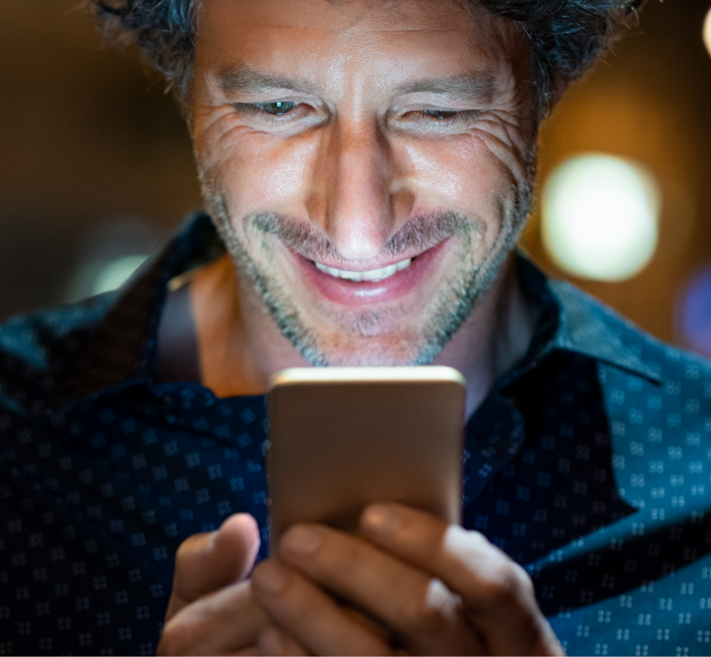 Man holding a phone and smiling at the screen which illuminates his face