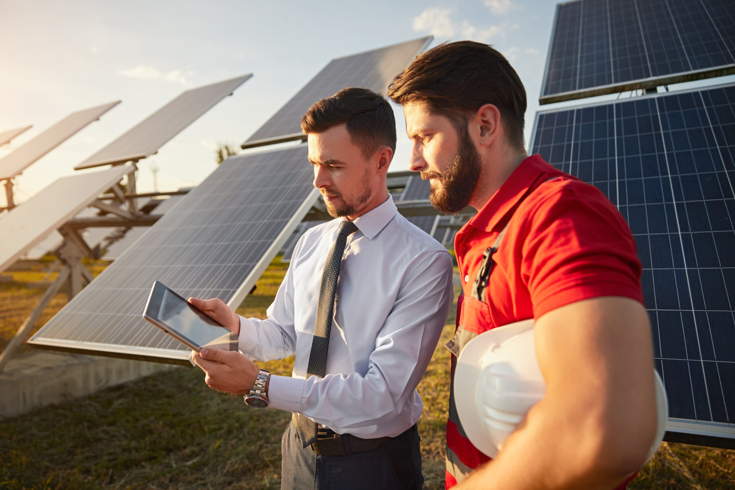 Focused male supervisor sharing tablet with technician near solar panels